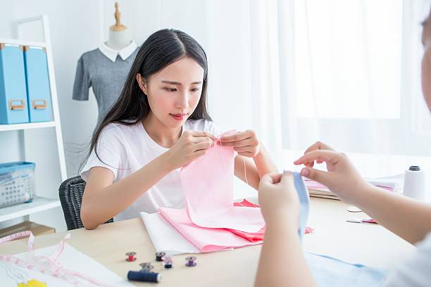 Sewing project in progress: two people handling fabric and tools at a well-lit table.