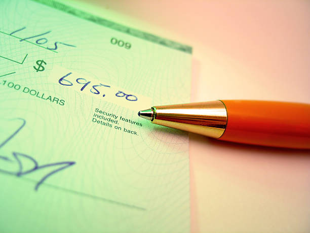 Close-up of a green check with the amount “695.00” written in blue ink and an orange-gold pen placed diagonally, illustrating how to write a cheque with proper details and security features.